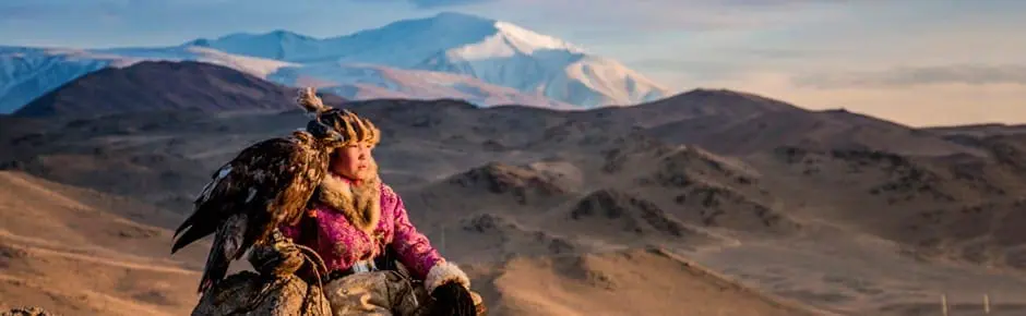 Photo of Individual wearing traditional clothing with an eagle perched on their arm in a mountainous area. | Wander Sober
