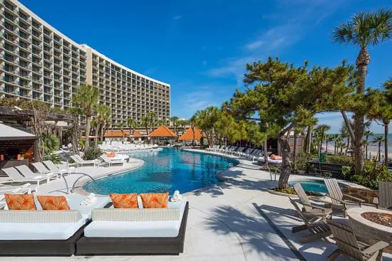 Photo of Swimming pool area featuring lounge chairs and palm trees at a hotel. | Wander Sober