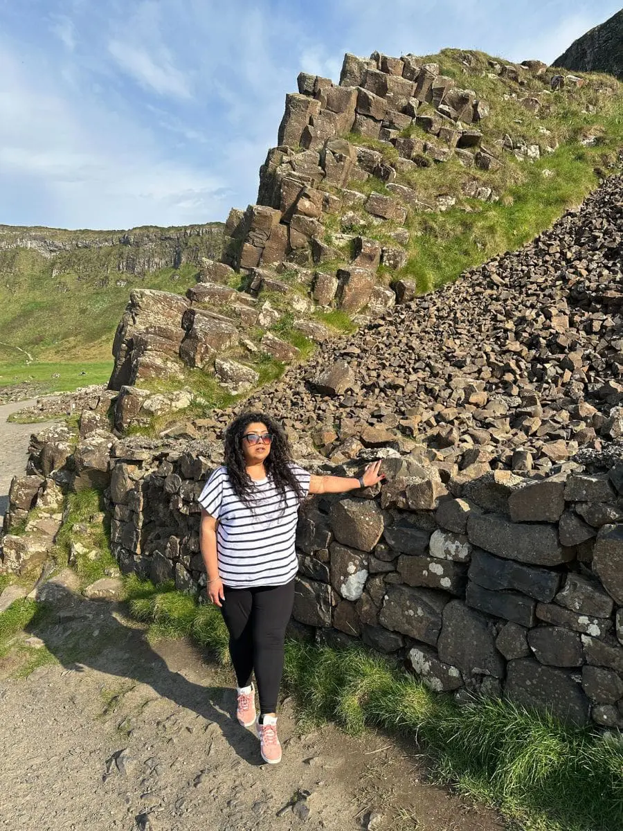 Photo of Individual wearing a striped shirt and sunglasses standing beside a rocky landscape with grass. | Wander Sober