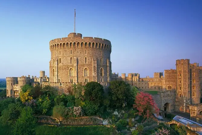 Photo of Windsor Castle, a historic royal residence, featuring its round tower and surrounding gardens under a clear sky. | Wander Sober