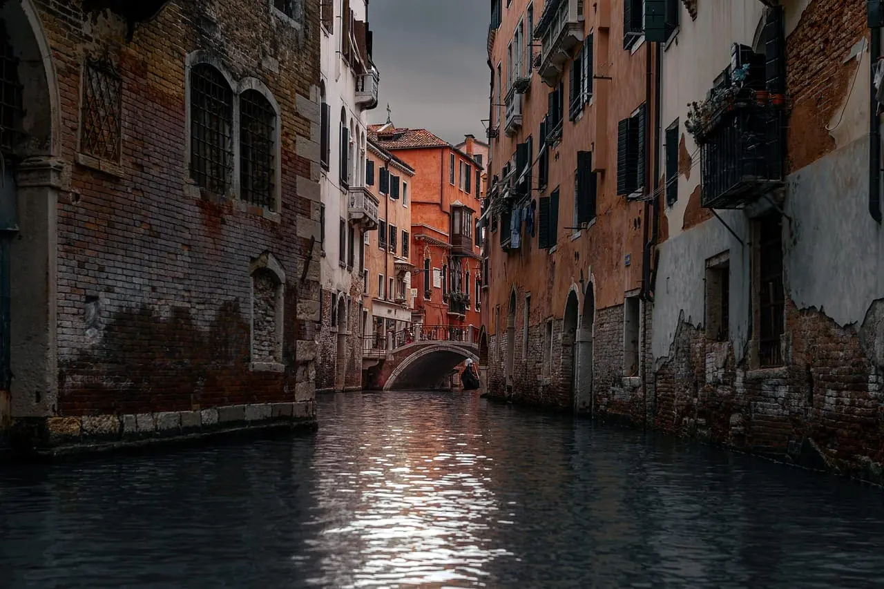 Narrow canal in Venice lined with historic buildings and a small bridge in the background.