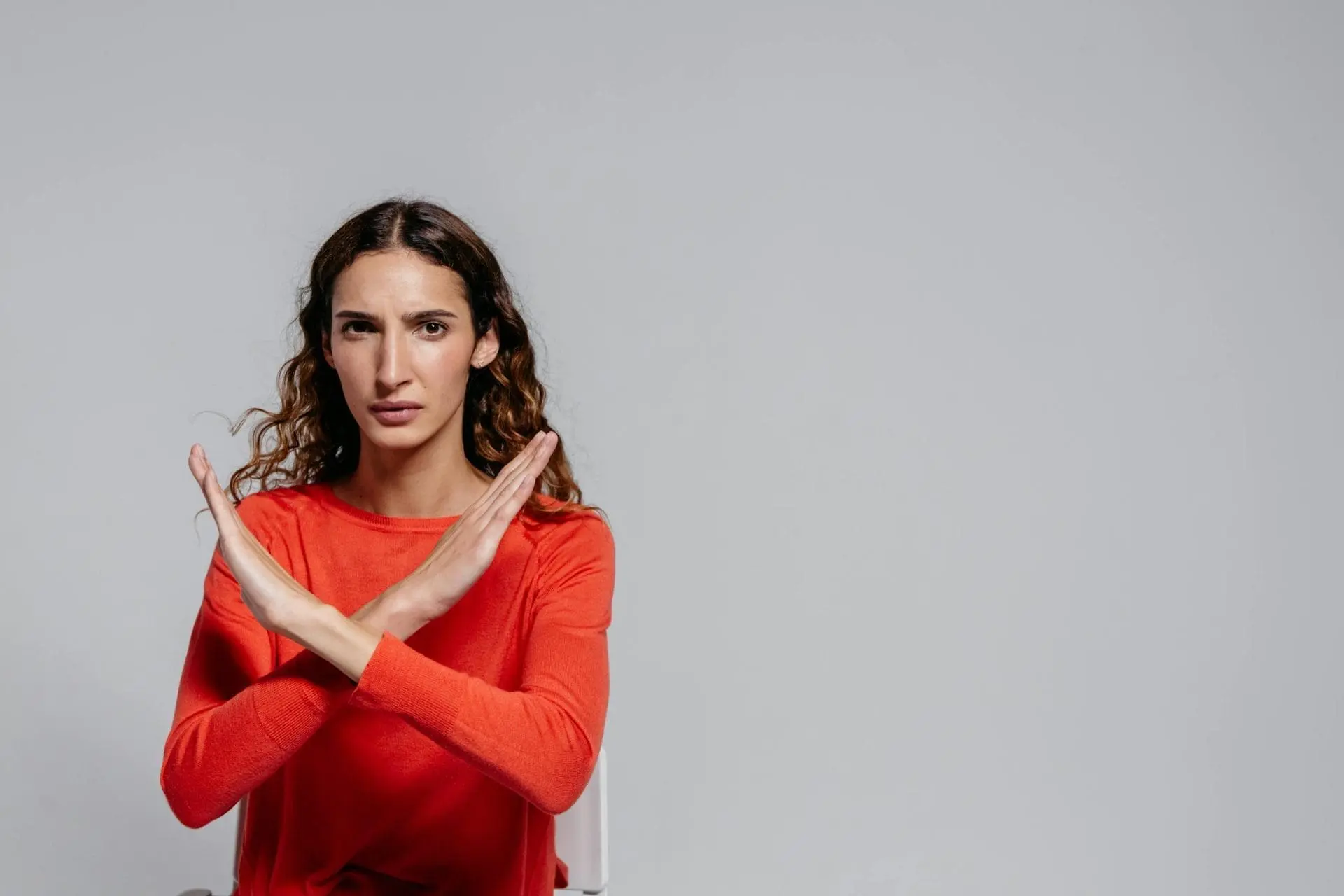 A woman in a red long-sleeve shirt making a gesture with her hands in a neutral setting.