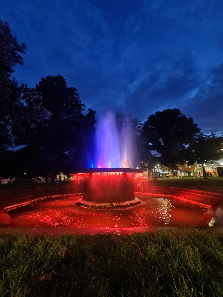 ADHD and how it manifests in me 3 Fountain illuminated with red and blue lights at night, surrounded by trees, reflecting a serene atmosphere for sober travel.