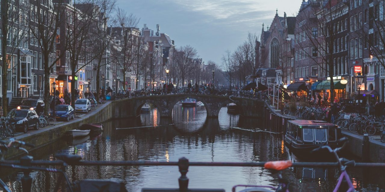 Amsterdam Sober: Canals, Art, and Non-Alcoholic Bars - Finding Joy in the City's Alcohol-Free Renaissance that Awakened My Senses 5 **Alt Text:** A serene evening view of a canal in Amsterdam, lined with trees and historic buildings. **Caption:** Experience the tranquil beauty of Amsterdam's canals, perfect for mindful exploration and relaxation. **Image Description:** A picturesque canal scene in Amsterdam at dusk, showcasing charming architecture and a peaceful atmosphere.