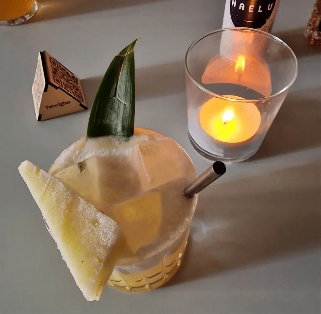 Photo of Cocktail with pineapple garnish, straw, and a candle in the background on a table. | Wander Sober