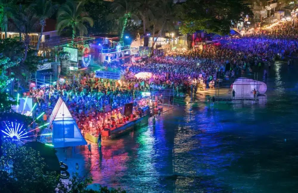 Vibrant full moon party scene in Thailand, featuring a large crowd celebrating on the beach with neon lights and lively atmosphere.