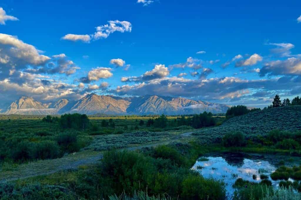 Photo of Scenic view of mountains under a blue sky with clouds and a small pond in the foreground. | Wander Sober
